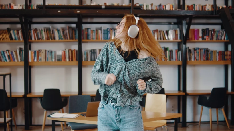 young-female-student-listens-to-music-on-headphones-and-dances-in-the-library-a-girl-i-sbi-351465547jpg_U3LcIN.webp